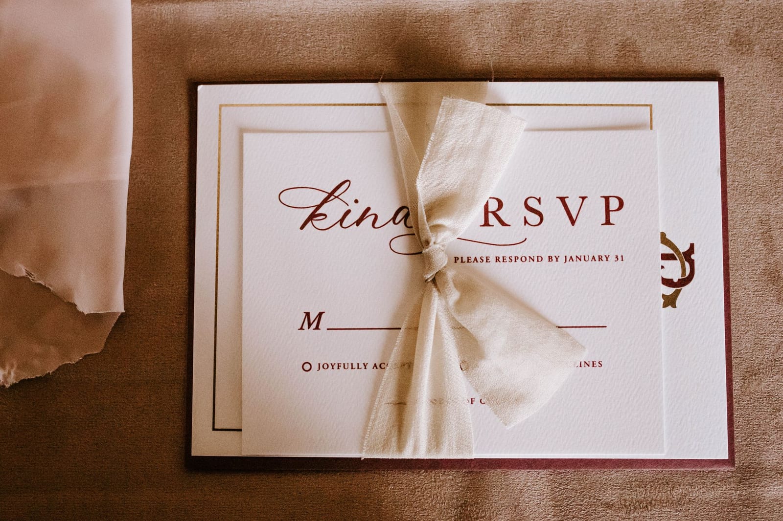 A reply card reading "Kindly RSVP, please respond by January 31" with an M___ line and accept or decline boxes, tied with a ribbon