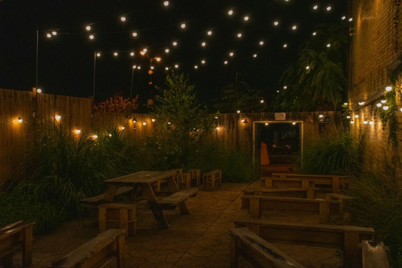 A courtyard of wooden picnic tables under strings of lights at night