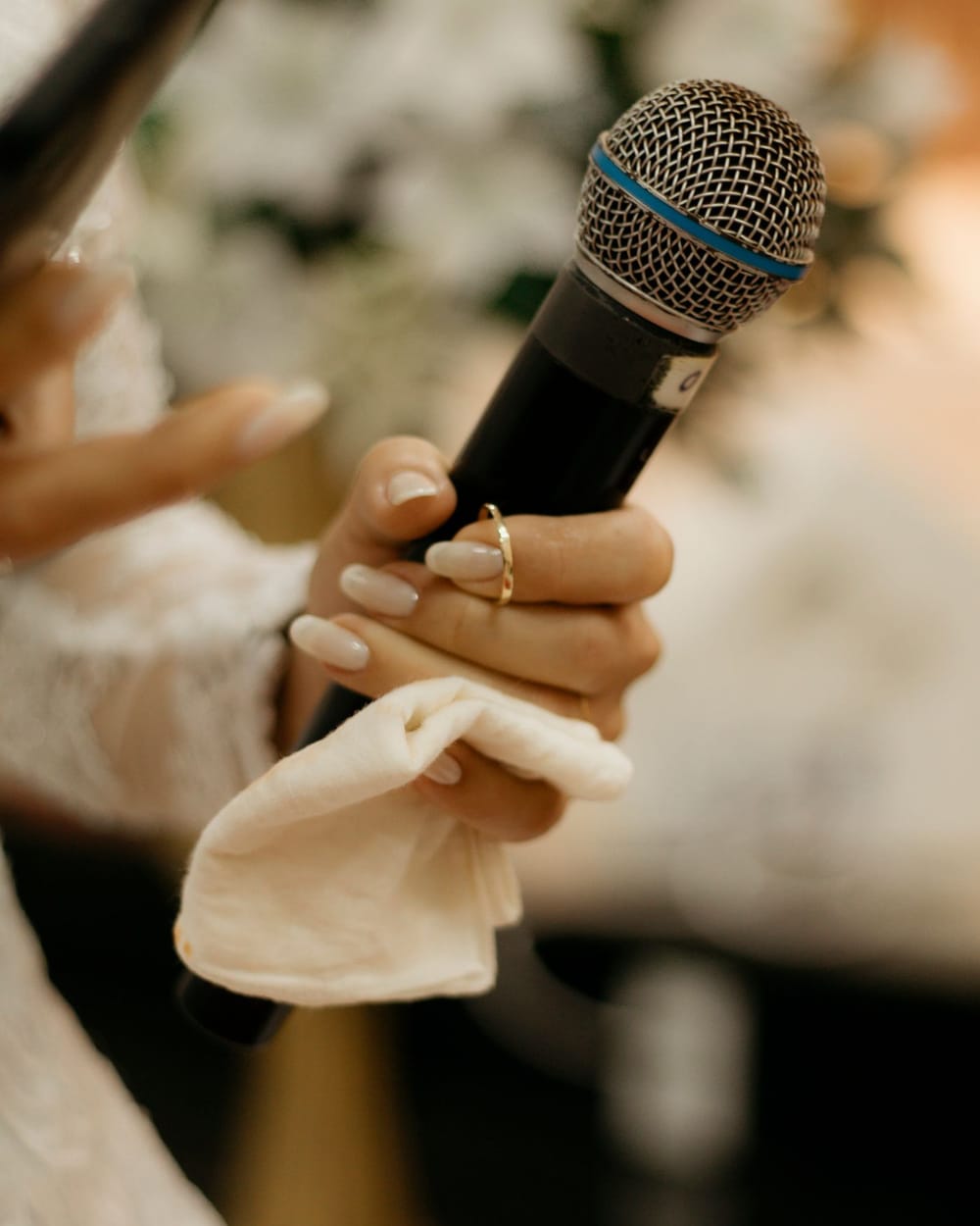 A hand with a gold wedding band holds a microphone and a folded white handkerchief