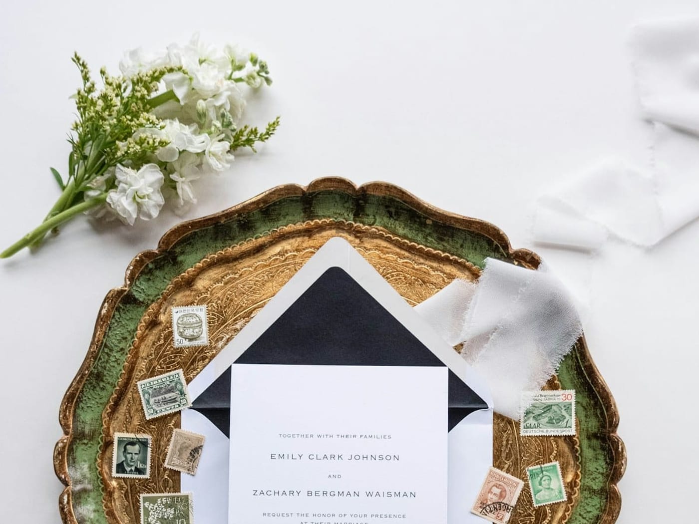 A wedding invitation in a black-lined envelope with vintage postage stamps on a gold tray