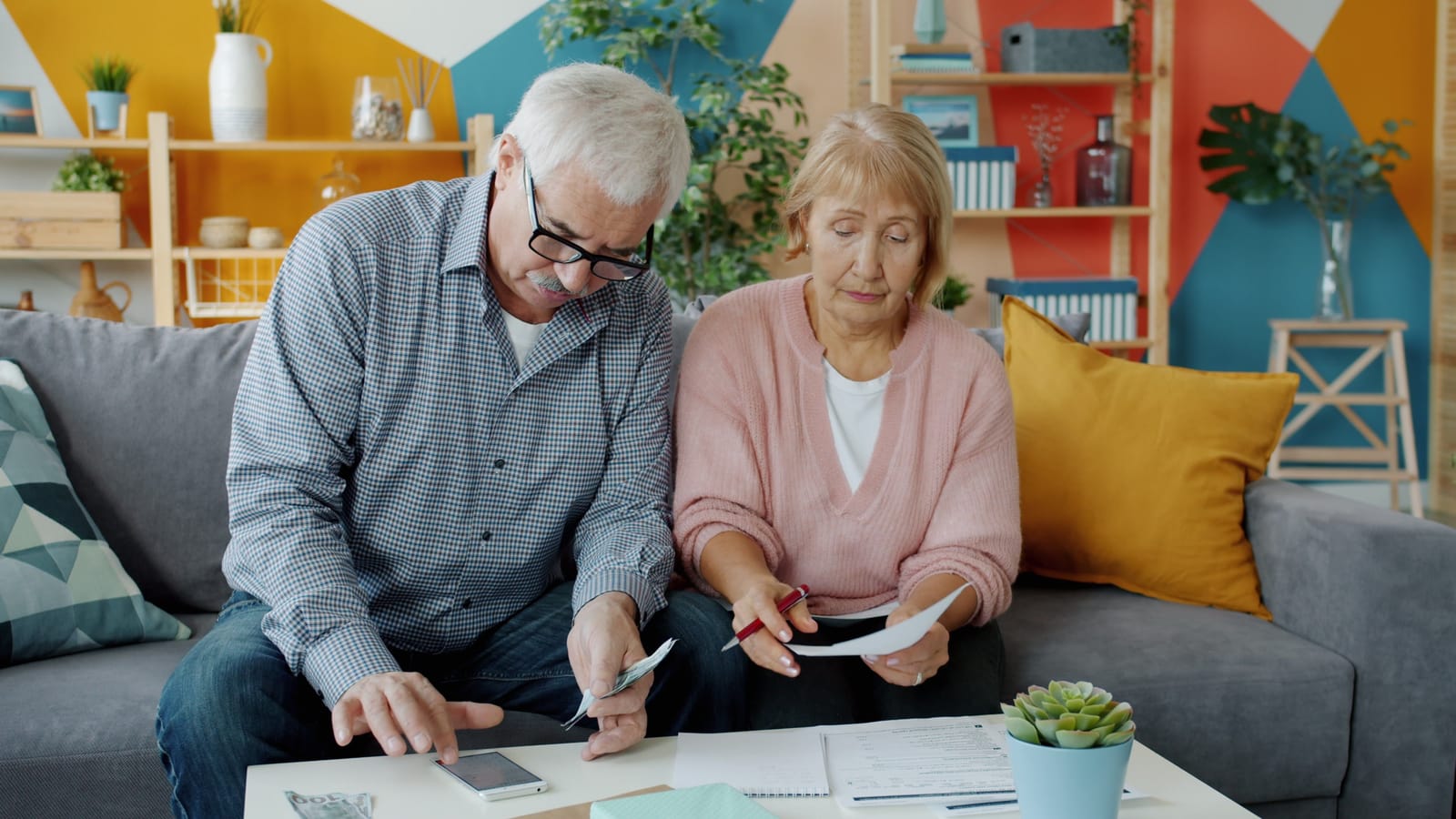 A grey-haired man and woman on a sofa going through papers, with a calculator and a phone on the coffee table