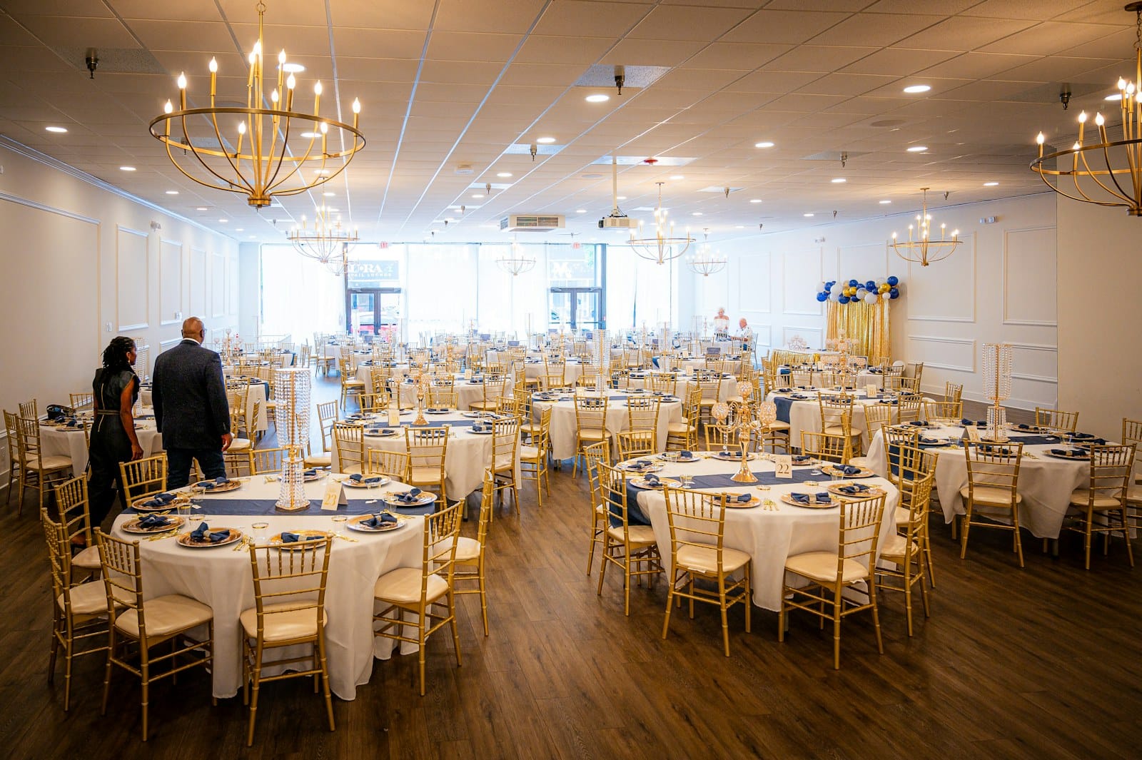 A ballroom wedding venue set with round tables, gold chairs and chandeliers before guests arrive