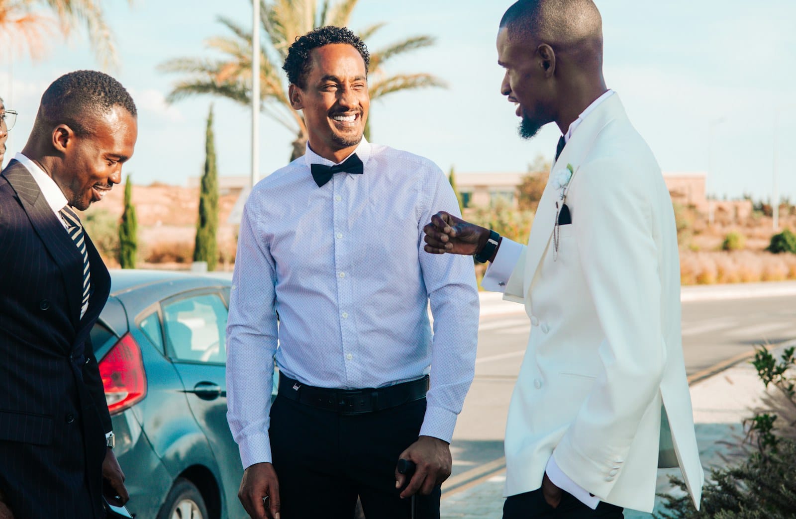 Three groomsmen in suits laughing together outdoors under palm trees