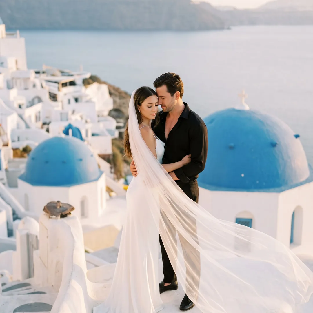 AI-generated pre-wedding photo example: couple on a Santorini rooftop above blue-domed churches at golden hour
